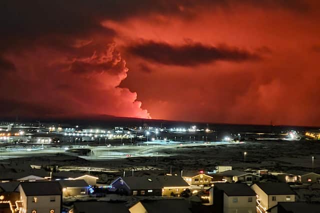 Houses in the village of Hafnarfjordur is seen as smoke is billowing in the distance as the lava colour the night sky orange from an volcanic eruption on the Reykjanes peninsula, western Iceland on December 18, 2023