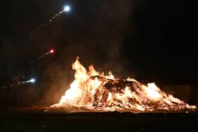 Fireworks light the sky over a large bonfire.