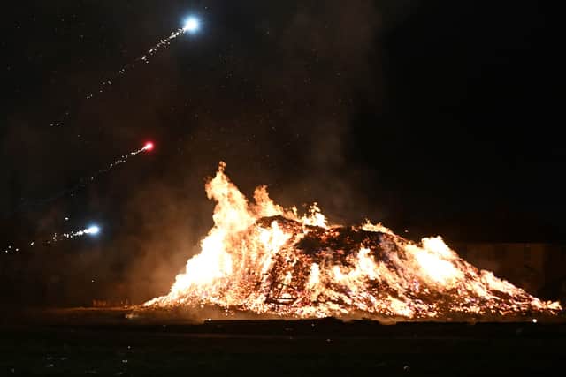 Fireworks light the sky over a large bonfire.