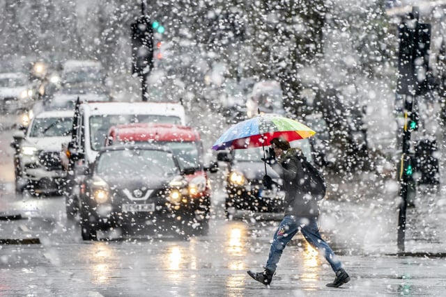 A woman with a bright umbrella crosses the road in York amid a flurry of snow