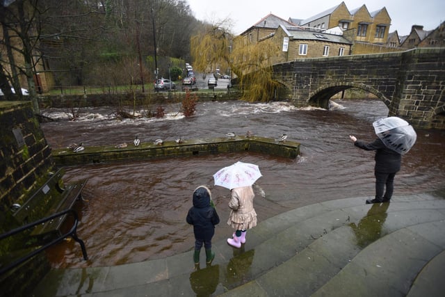 People stand on steps leading to a footpath alongside the river Calder, now flooded after persistent heavy rain, in the centre of Hebden Bridge, West Yorkshire. [Image: Asadour Guzelian]