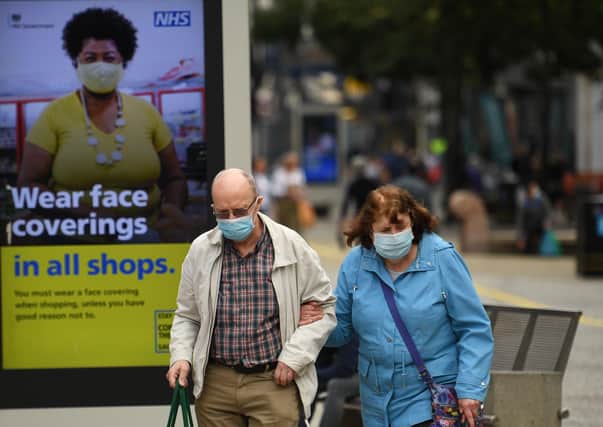 Shoppers wearing face masks walk past a sign calling for the wearing of face coverings in shop (Photo by OLI SCARFF/AFP via Getty Images)
