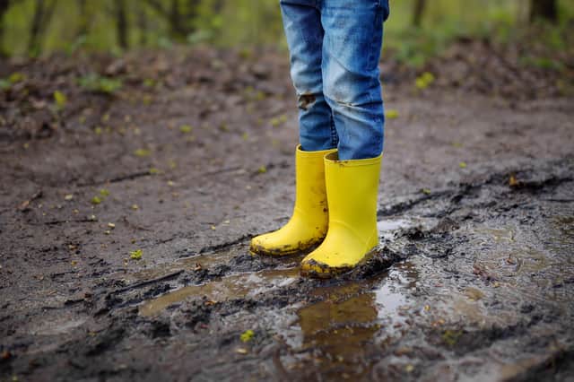 Mischievous preschooler child wearing yellow rain boots walking by muddy road. By Shutterstock