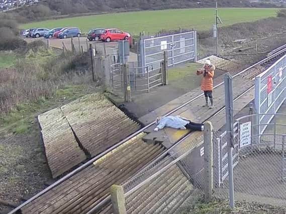 A person takes a photo of a woman lying on the tracks. Picture via Network Rail