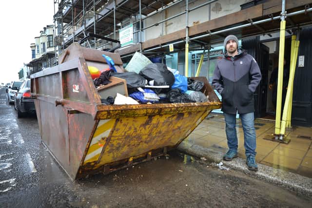 Graeme Williams is pictured next to the skip that's obscuring his shop front, White Rock, Hastings. SUS-210302-114350001