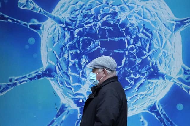 OLDHAM, UNITED KINGDOM - NOVEMBER 24: A man wearing a protective face mask walks past an illustration of a virus outside Oldham Regional Science Centre on November 24, 2020 in Oldham, United Kingdom. England is continuing its second national coronavirus lockdown. People are still permitted to exercise with one other person, takeaway food is permitted but bars and restaurants are shut for sit-in service. Schools will remain open but people are being advised to work from home where possible and only undertake necessary travel. All non-essential shops are closed with supermarkets and builders' merchants remaining open. (Photo by Christopher Furlong/Getty Images) NNL-201124-145747001