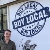 Artist Sam Johnson with his ‘Buy local’ mural in Robertson Street, next to the Bullet Cafe