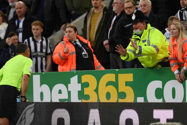 A police officer interacts with Match Referee, Andre Marriner as he shares information regarding the medical emergency occurring in the stand during the Premier League match between Newcastle United and Tottenham Hotspur at St. James Park