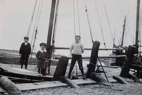 Three smart young men on a boat at Bosham Quay in about 1909. It poses a mystery, as the tide has gone out yet the boat is near the top of the quay. Was the boat on the deck of a much larger craft?