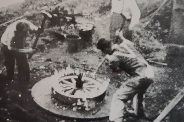 Fred Stacey watching his son Frederick and John Kerley in the early 1940s as they hammer a heated iron tyre on a cartwheel prior to dousing it with water to cool and shrink it on the felloes.