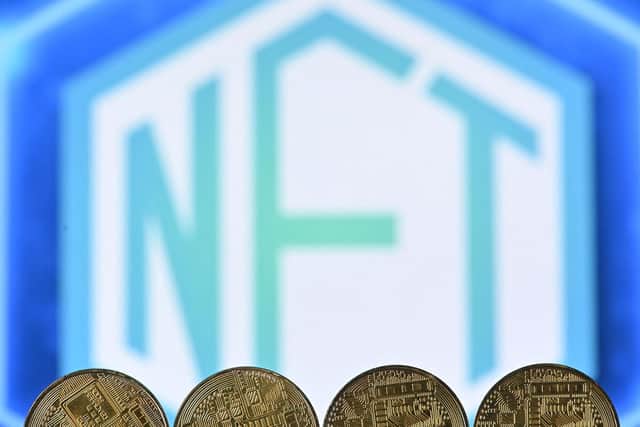 An illustration picture taken in London on December 30, 2021, shows gold plated souvenir cryptocurrency coins arranged by a screen displaying a NFT (Non-Fungible Token) logo