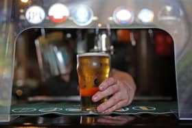 Barman wears PPE while pouring a pint behind a protective shield at the bar as the lifting of further lockdown restrictions in England comes into effect