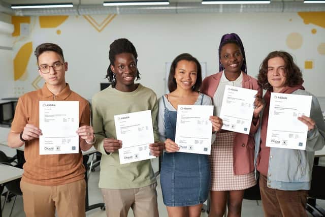 Diverse group of young people standing in school classroom smiling happily at camera and holding test certificates, copy spaceOrange Grove Foster Care has partnered with an education charity ASDAN SUS-210706-114022001