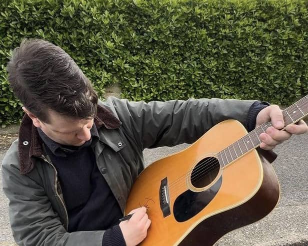 Jamie T signs an acoustic guitar ahead of a charity raffle.