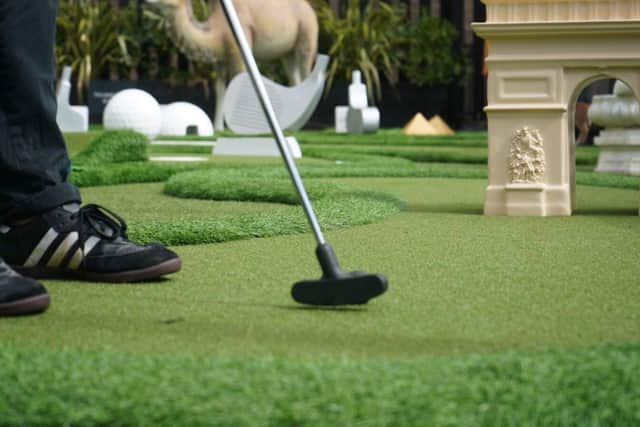 A picture of a mini golf putter and ball about to be hit towards an obstacle.