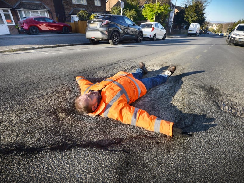 Councillor Andrew Crotty lying on top of a giant pothole in Buckhurst Road, Bexhill in April 2021.