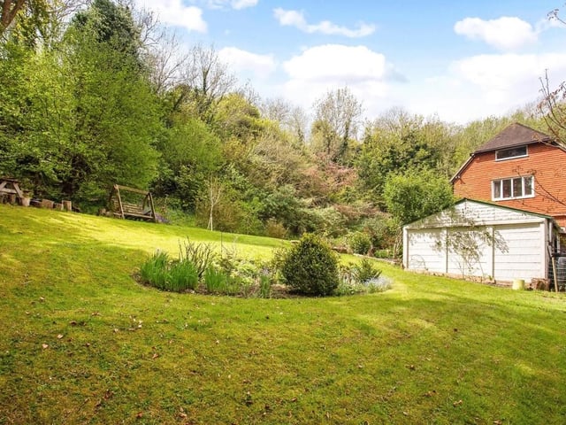 The south-facing rear garden has an expansive lawn with bedding plants and shrubs surrounded by mature trees and open woodland