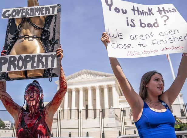 Abortion-rights supporter Sam Scarcello (L) and anti-abortion activist Elianna Geertgens hold competing signs in front of the Supreme Court while covered in fake blood on July 4, 2022 in Washington, DC (Photo by Nathan Howard/Getty Images)