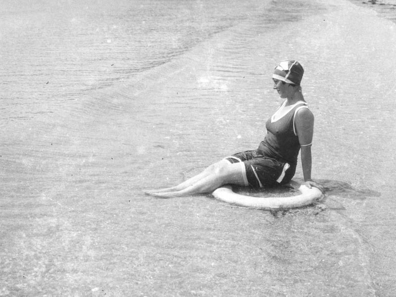 A woman sitting in a lifebelt enjoys the lapping of the waves on Littlehampton beach, circa 1925.