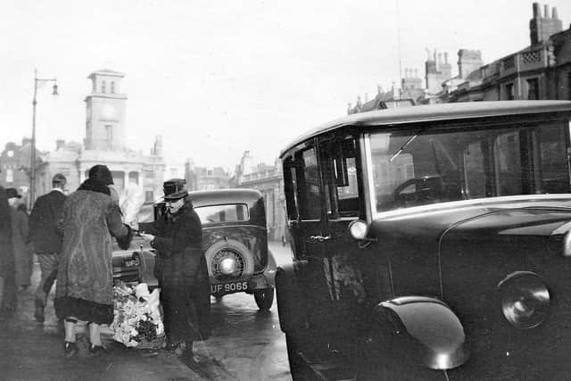 A flower seller among the cars parked in South Street, Worthing, on Christmas Eve, 1932. In the background is the old Town Hall, opened in 1835 and demolished to make way for the Guildbourne Centre in 1968. Picture: Frank Hooper