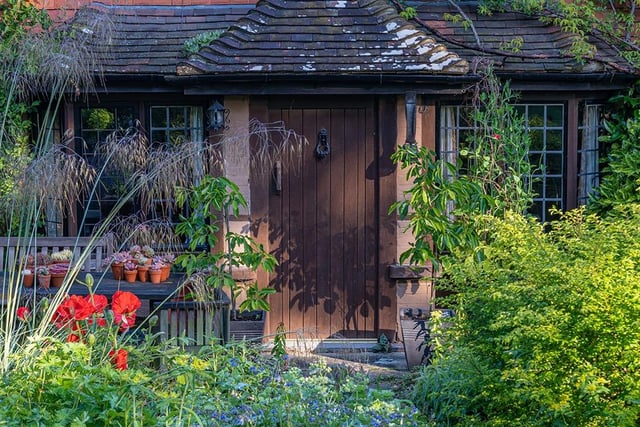 View of perennials and shrubs in an informal country cottage garden border at the front of a house in Summer - June