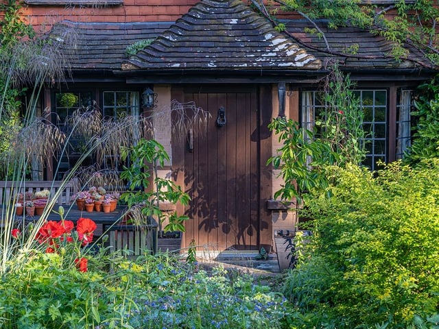 View of perennials and shrubs in an informal country cottage garden border at the front of a house in Summer - June