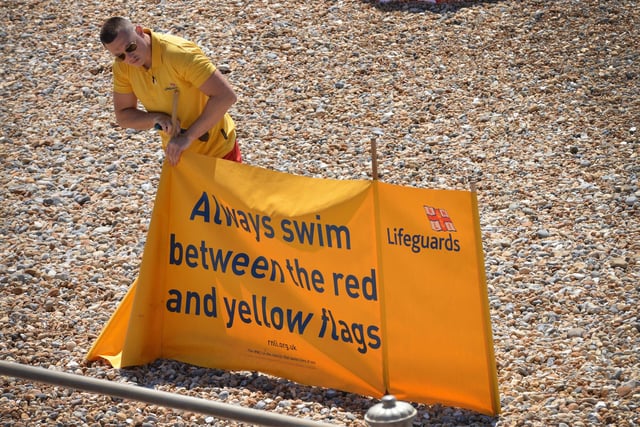 Hastings and St Leonards seafront pictured during the mini heatwave on July 10 2022. A lifeguard is pictured setting up a swimming safety banner.
