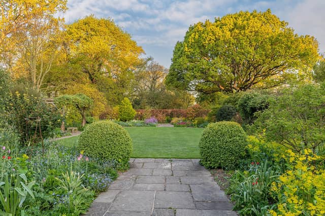 View 0f a symetrically designed country cottage garden with mixed borders flowering in Spring by John Glover