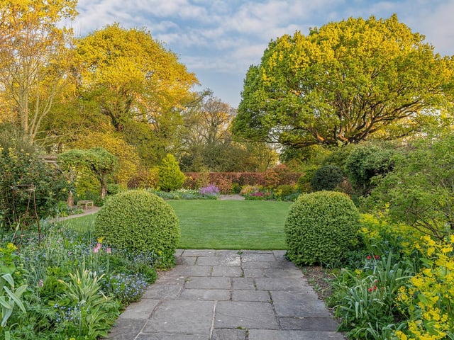 View 0f a symetrically designed country cottage garden with mixed borders flowering in Spring by John Glover