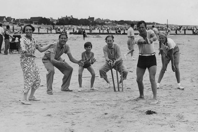 English comic actor Claude Hulbert (behind wicket) and entertainer Bobby Howes (batting) playing cricket on the beach during a family holiday in Felpham, West Sussex on 11th August 1934. On the right is Pamela Hulbert, daughter of Claude's brother Jack Hulbert and actress Cicely Courtneidge, who are also on the holiday. On the left is Claude's wife, actress Enid Trevor.