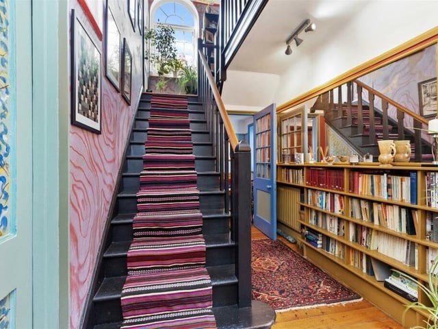 The entrance hall has book shelves and original artwork alongside solid oak stairs to the first floor