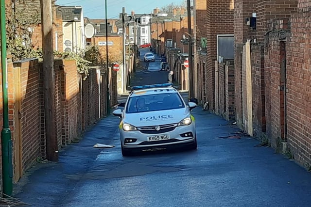 A police vehicle remains on duty in a back lane behind the street.