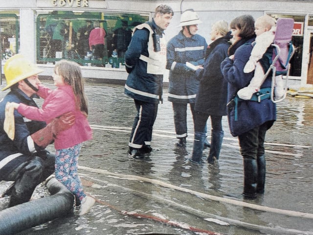 Firemen take press enquiries while one demonstrated a 'fireman's lift' for a young girl.