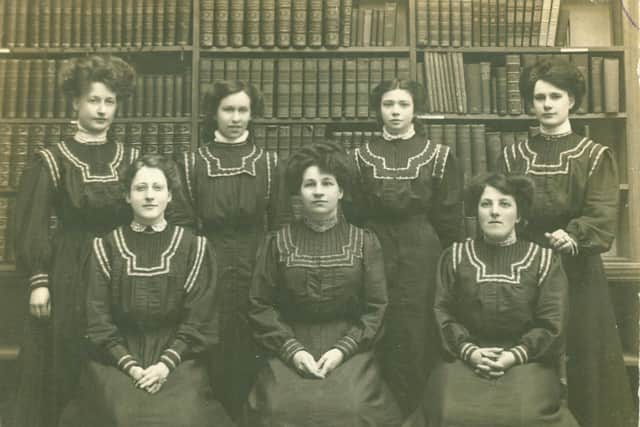 Worthing Library Staff in 1909. Female staff members of Worthing Public Library pose in front of bookshelves. All are wearing their winter overalls with long skirts and sleeves, and pin-tucked or pleated bodices. Identified are: Deputy Librarian (later Librarian) Ethel Gerard (standing far left), and Librarian Marian Frost (seated, centre). Seated at right is possibly Miss Paine, and standing at far right is possibly Dorothy Moss.