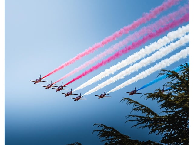 The Red Arrows fly over Goodwood, trailing red white and blue.
