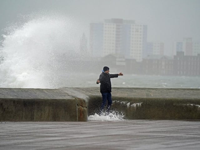 A pedestrian feels the strength of the wind as waves crash against the seafront in Southsea as Storm Barra hit. Picture: Andrew Matthews/PA Wire
