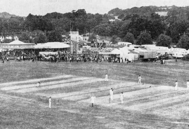 A picture from the 1960s showing a funfair taking place while a cricket match is in play on Broadwater Green