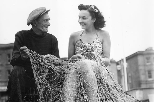 Fisherman Charlie Parsons gets some unexpected help mending his nets from holidaymaker Margaret Blenksby on Worthing beach in July 1946