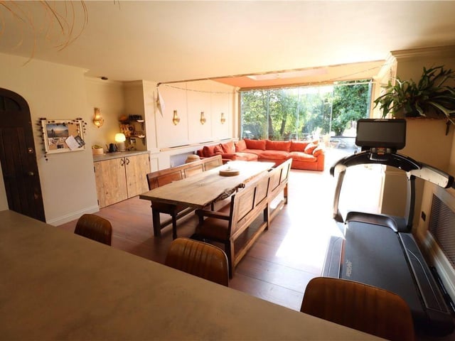 The living and dining areas are flooded with natural light through a skylight and frameless floor-to-ceiling glass curtains
