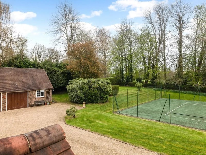 Outside there is a large hard tennis court and a large double garage block