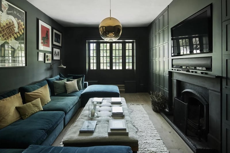 An intimate sitting room features a slate chimneypiece and an open fire, surrounded by contemporary panelled cupboards