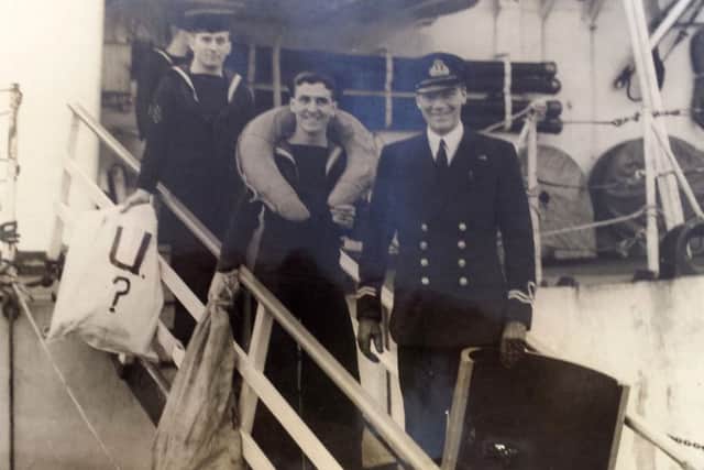 Tom (centre) disembarking from a warship holding a bag of U-boat wreckage