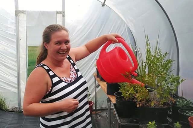 A herbalist working in a stuffy polytunnel is surrounded by plants wilting at 45Â°C