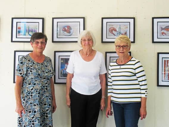 Worthing Twinning Association members Val (Chair),  Pam (Secretary) and Sybile (German co-ordinator) standing  in front of the paintings by Peter Seip