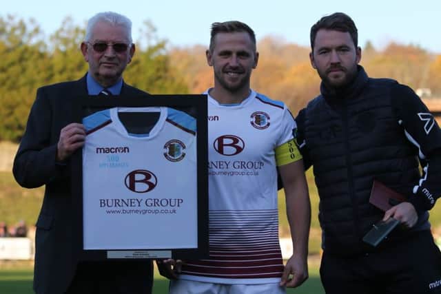 Hastings United captain Sam Adams receives a framed shirt from president Dave Ormerod (left) and manager Chris Agutter (right) in recognition of his 500 appearances for the football club. Picture courtesy Scott White