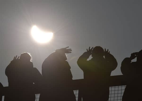 People, with special glasses, watch as an eclipse of the sun begins over the Eden Project near St Austell in Cornwall. Photo: Ben Birchall/PA Wire.