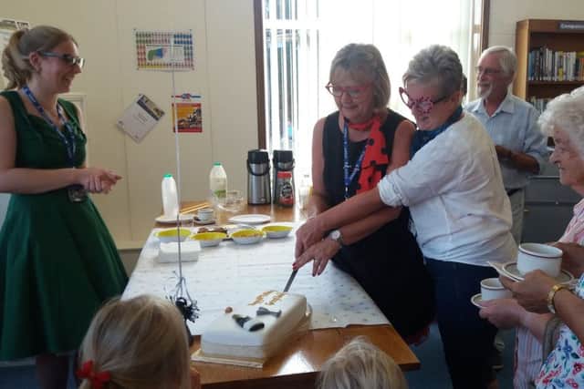 Samantha Herron and Tina Green cut the cake, watched by community librarian Lyndsey Power, left