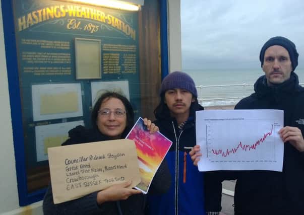 Members of Fossil Free Hastings pose outside Hastings Weather Station with a copy of the WMO report. The graph shows global temperature changes since 1880