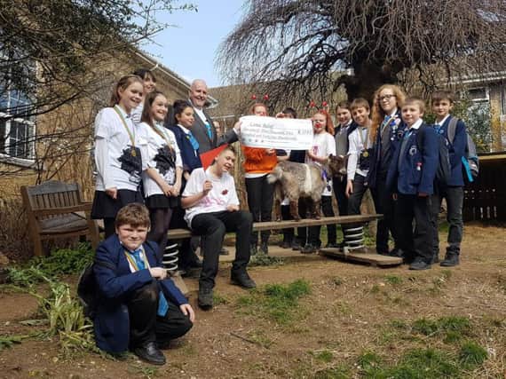 Headteacher William Aristide-Deighan with students and one of the school's pygmy goats, holding a cheque for Comic Relief